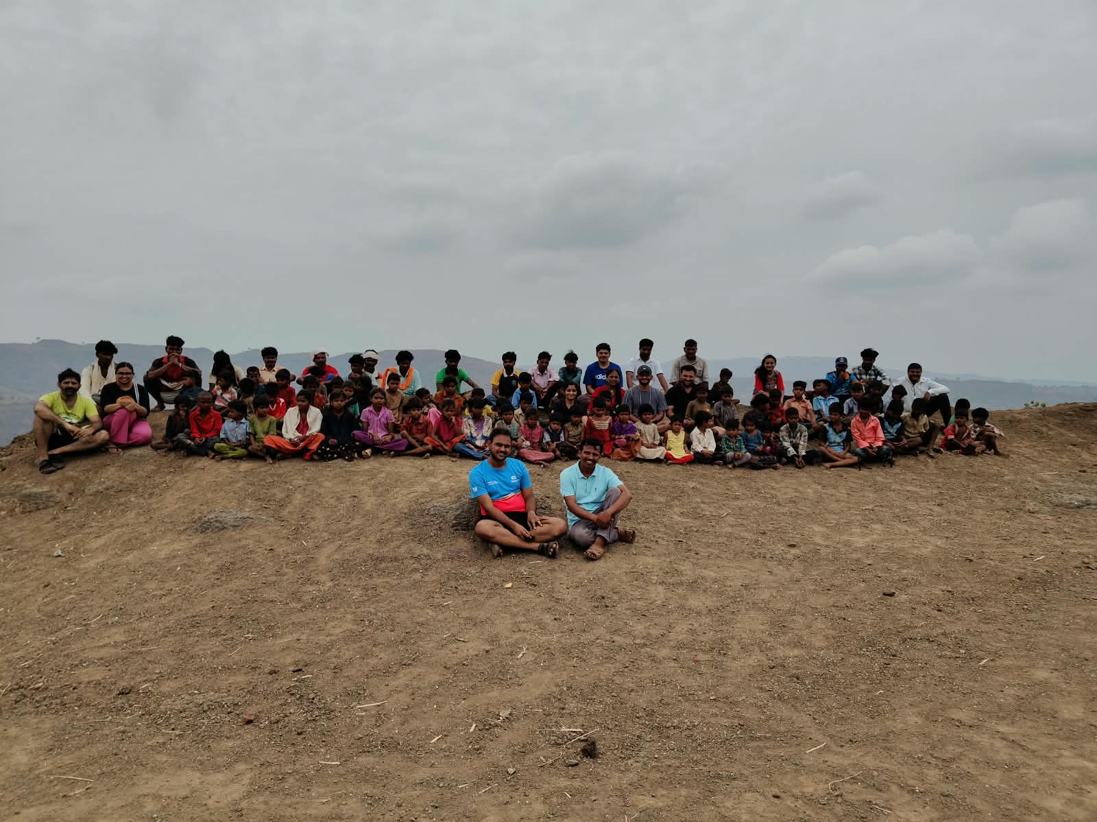 यंग फाऊंडेशनचे कार्यकर्ते आणि अनेक मुले सातपुड्यातील मोकळ्या मातीच्या जागेवर बसले आहेत.