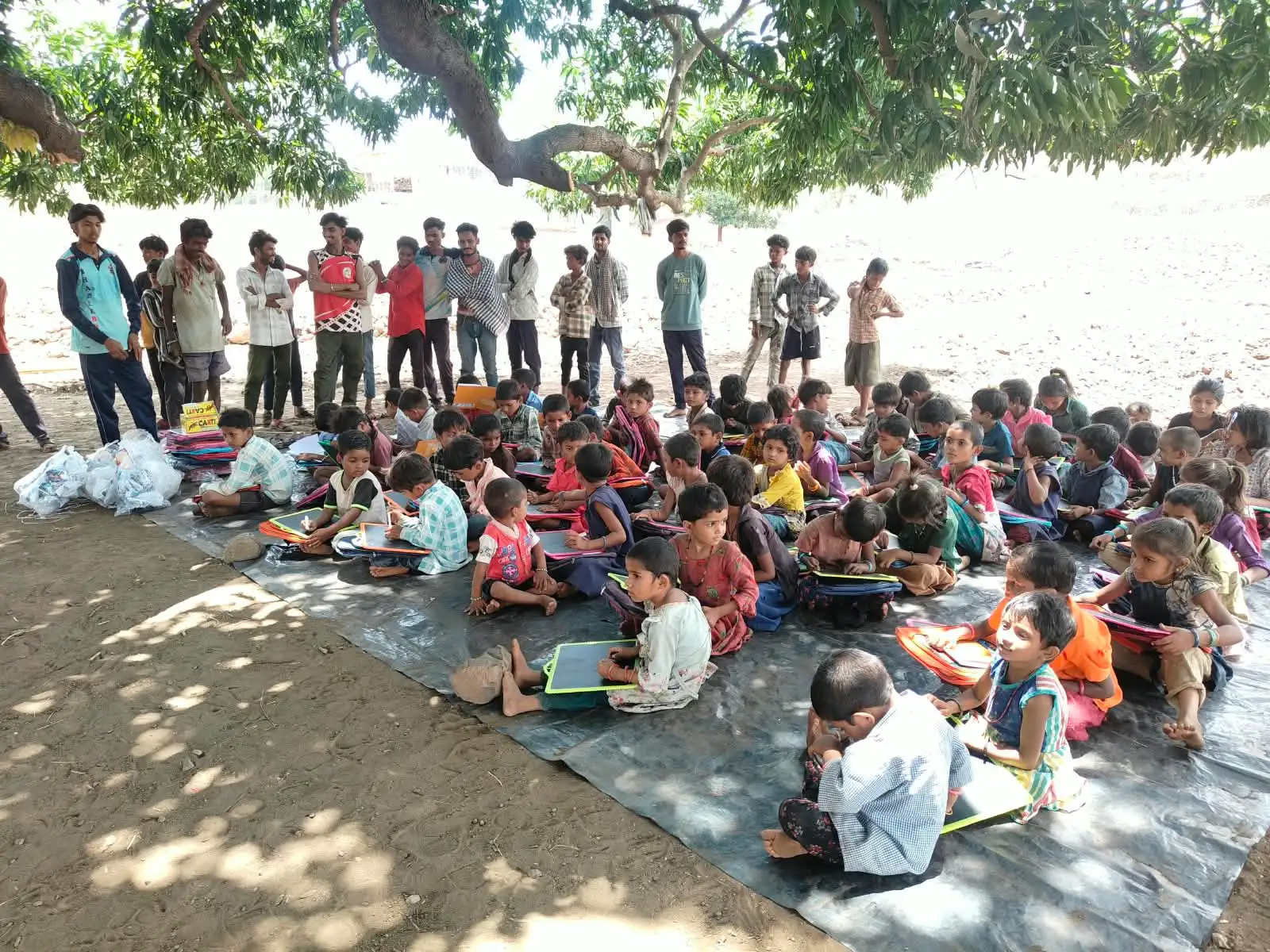 सतपुड्याच्या डोंगररांगांमध्ये झाडाखाली बसलेली मुले आणि मागे उभे असलेले तरुण.
