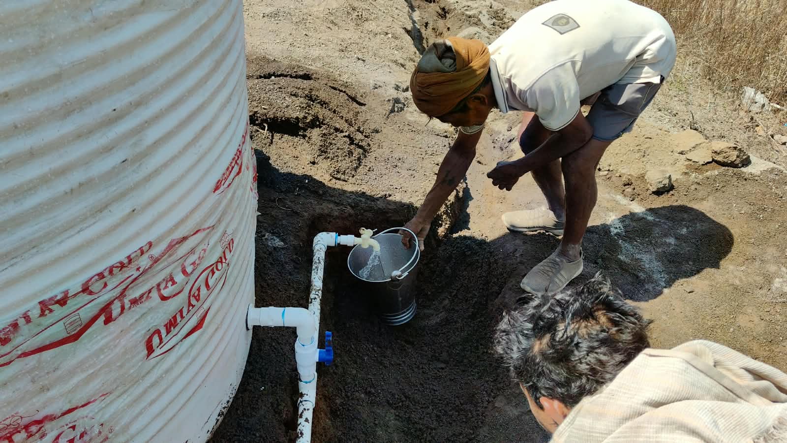 पाण्याच्या टाकीजवळ उभं राहून बादलीत पाणी भरणारी व्यक्ती.
