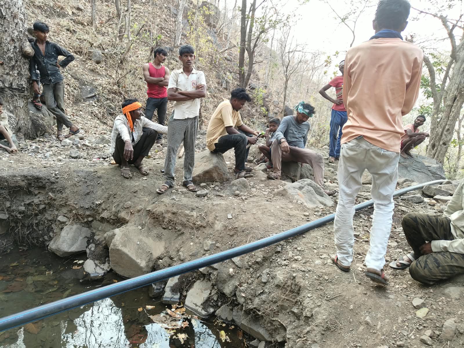 सतपुडा डोंगरातील जंगलात काळ्या पाइपजवळ काही लोक एकत्र जमले आहेत.