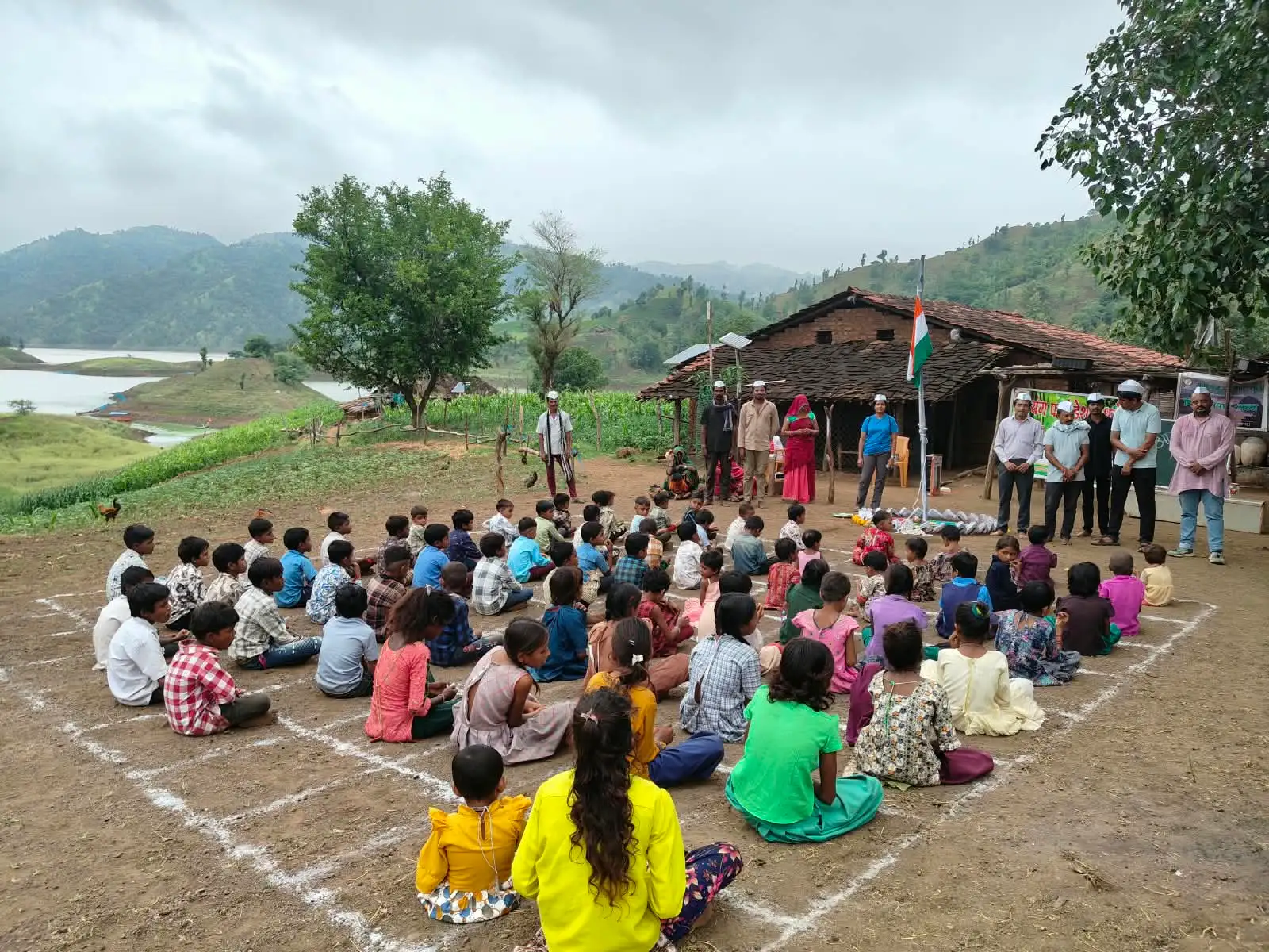 सतपुडा डोंगरांमध्ये एका घरासमोर मुले आणि लोक ध्वजवंदनासाठी जमले आहेत.