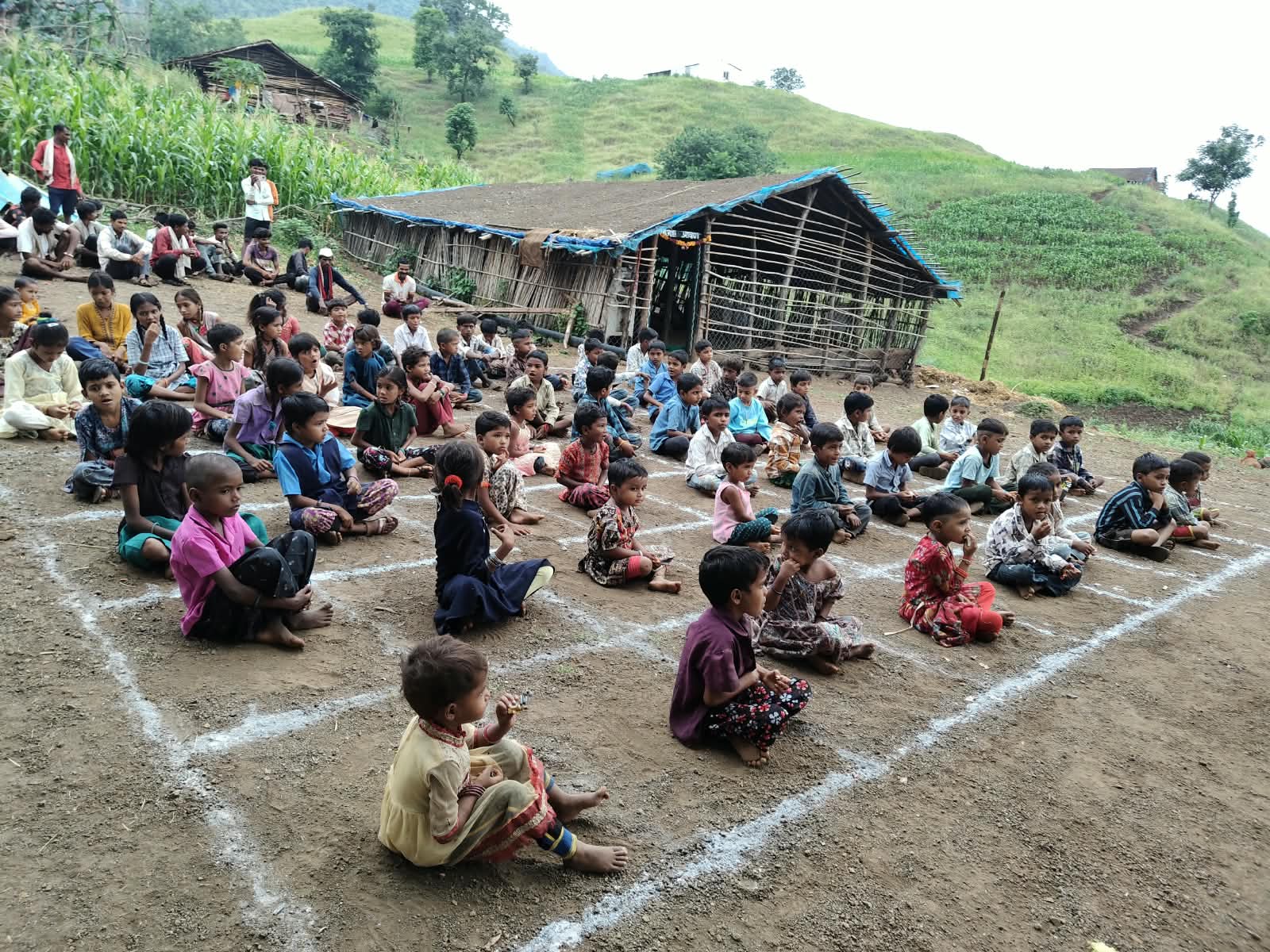 सतपुडा डोंगरामध्ये मुले जमिनीवर रेषा आखलेल्या जागेवर बसली आहेत.