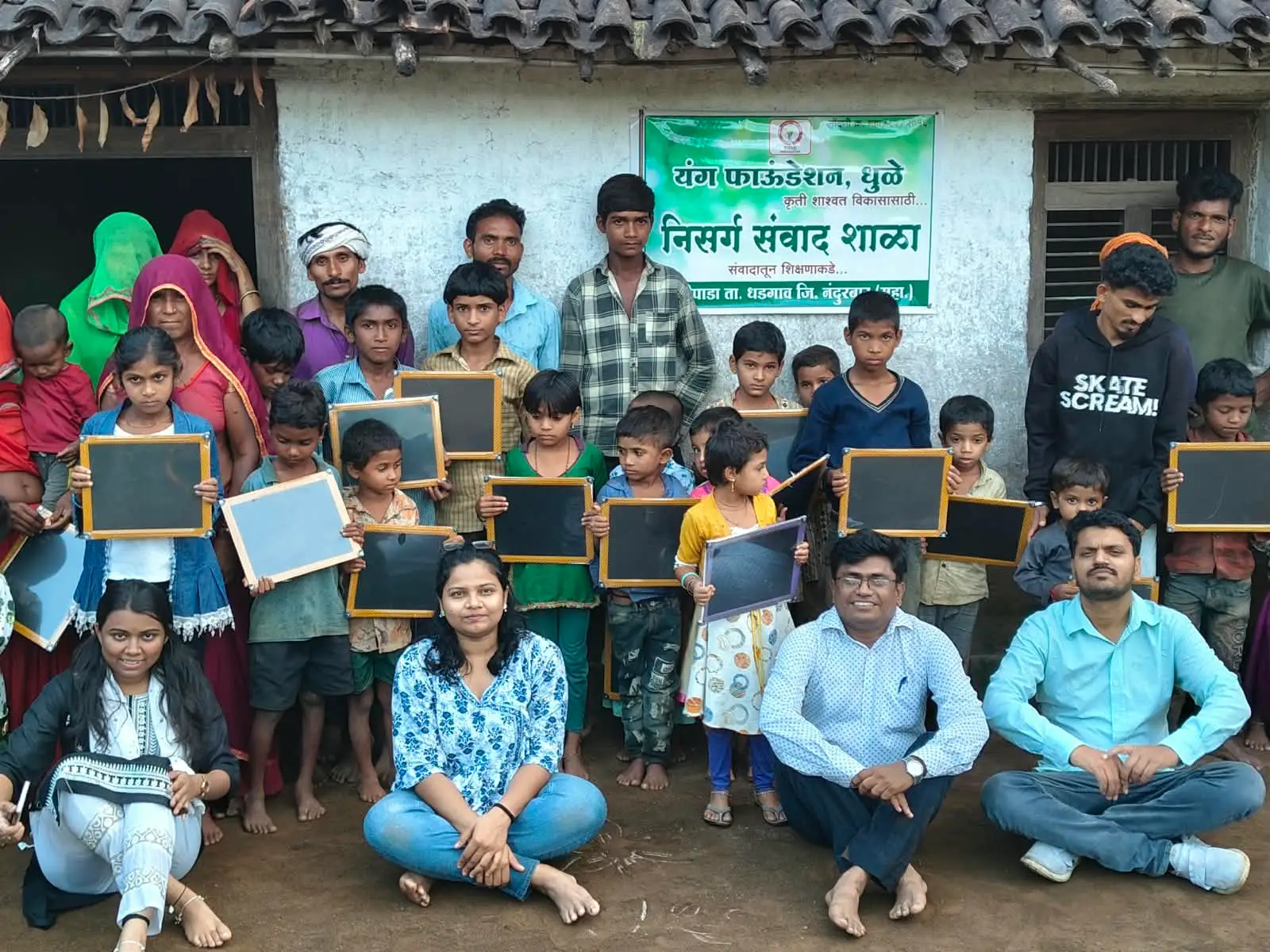 यंग फाऊंडेशनच्या निसर्ग संवाद शाळेत मुले आणि कार्यकर्ते ब्लॅकबोर्ड धरून उभे आहेत.