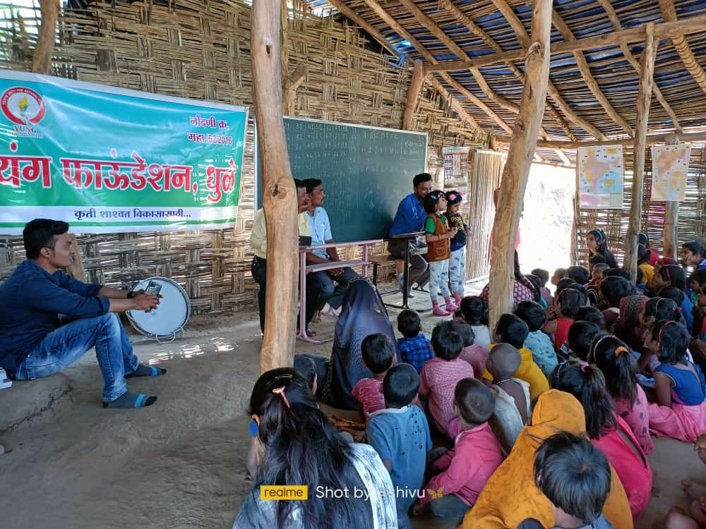 यंग फाउंडेशन, धुळे च्या कार्यक्रमात शेकडो मुले आणि शिक्षक बांबूच्या शेडमध्ये बसले आहेत.