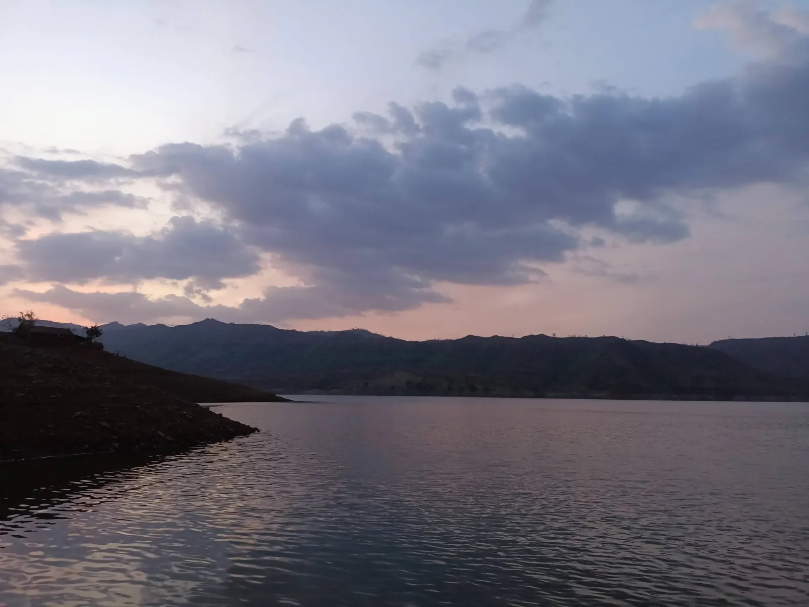 पाण्यावर सूर्यास्ताचे प्रतिबिंब पडलेले असून मागे डोंगर आहेत.