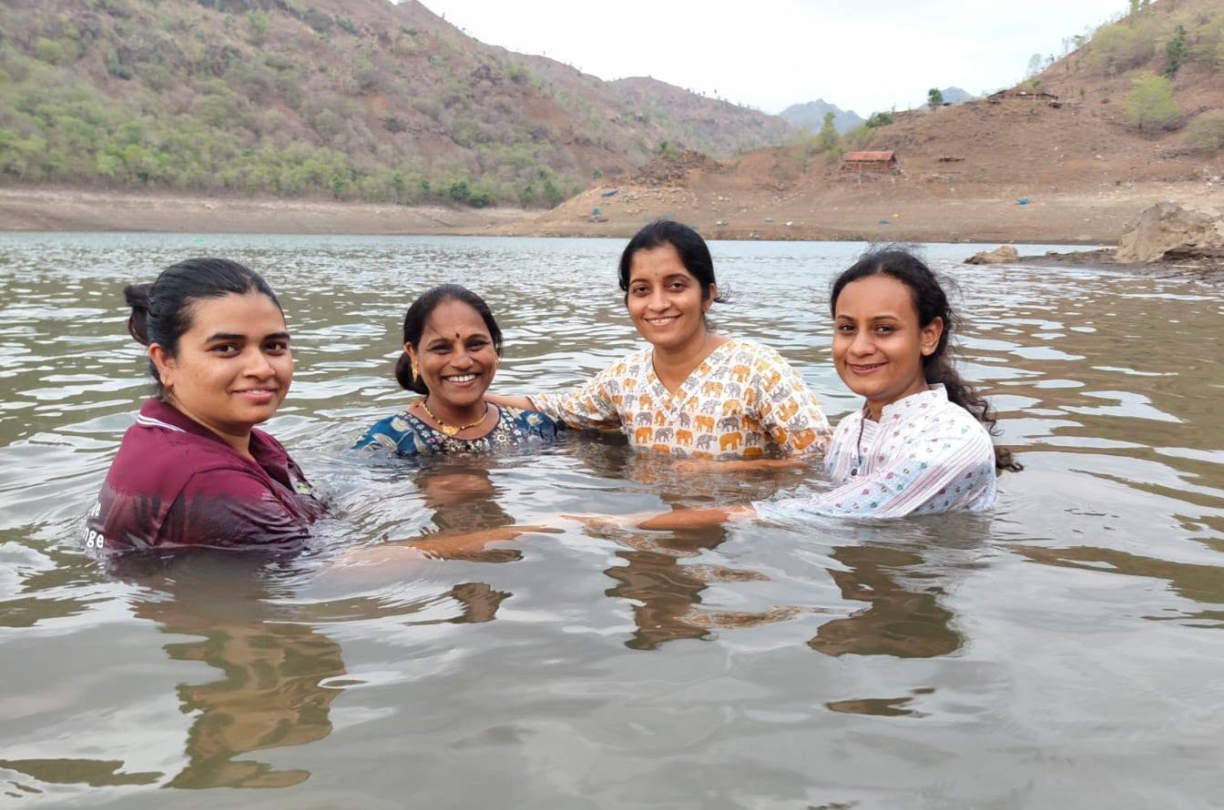 चार महिला पाण्यात उभे राहून हसत आहेत.