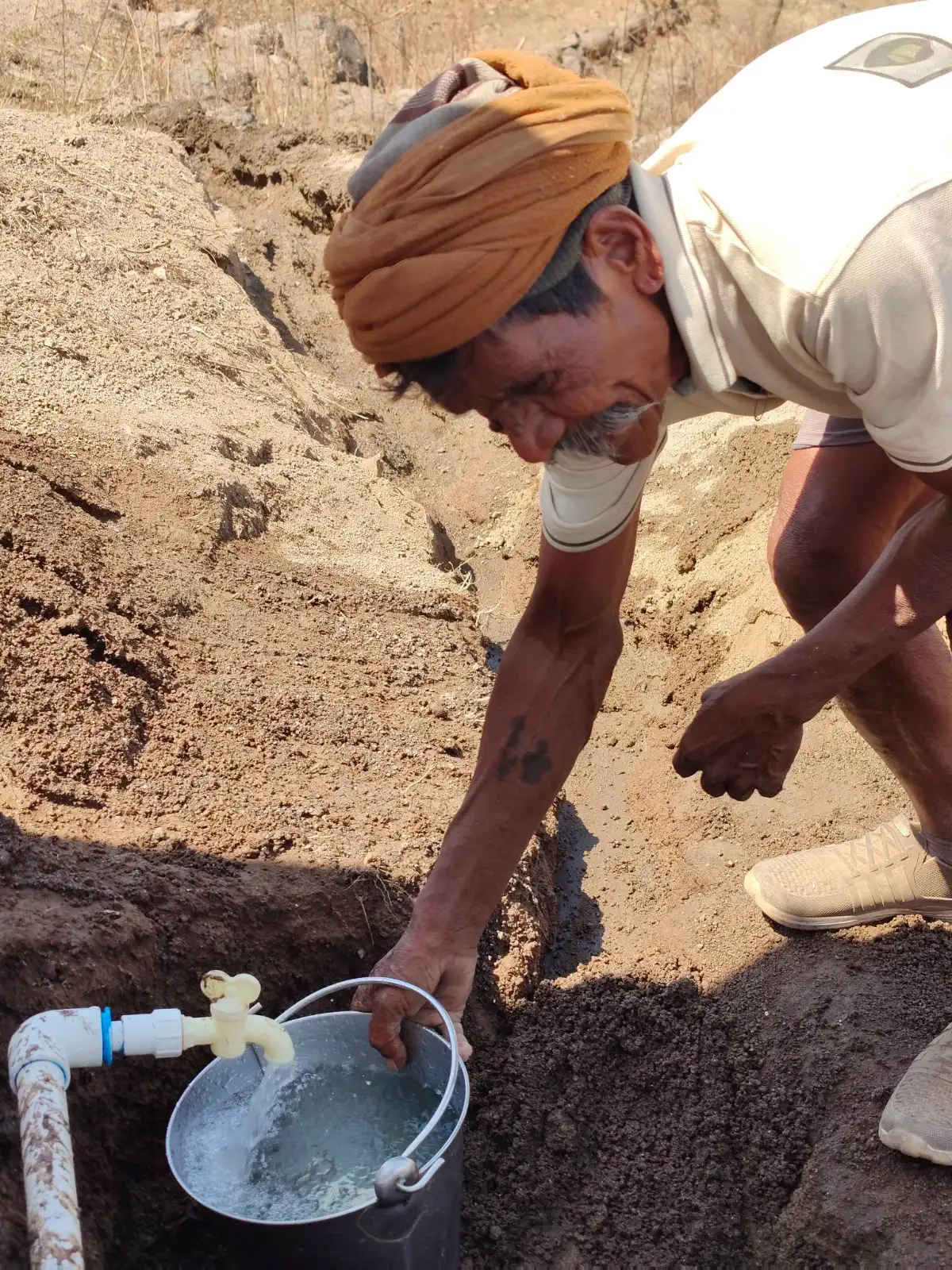 एक व्यक्ती सातपुडा भागात पांढऱ्या नळाखालील बाल्टीत पाणी भरत आहे.