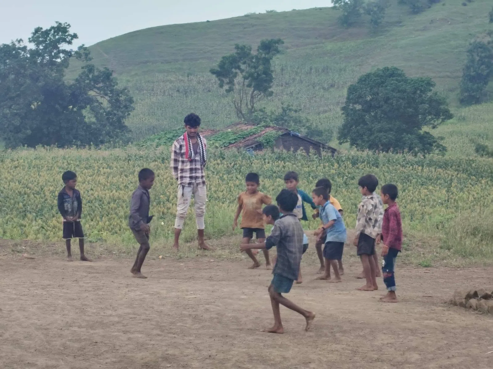 Children and a young man are playing on a ground in the Satpuda hills.